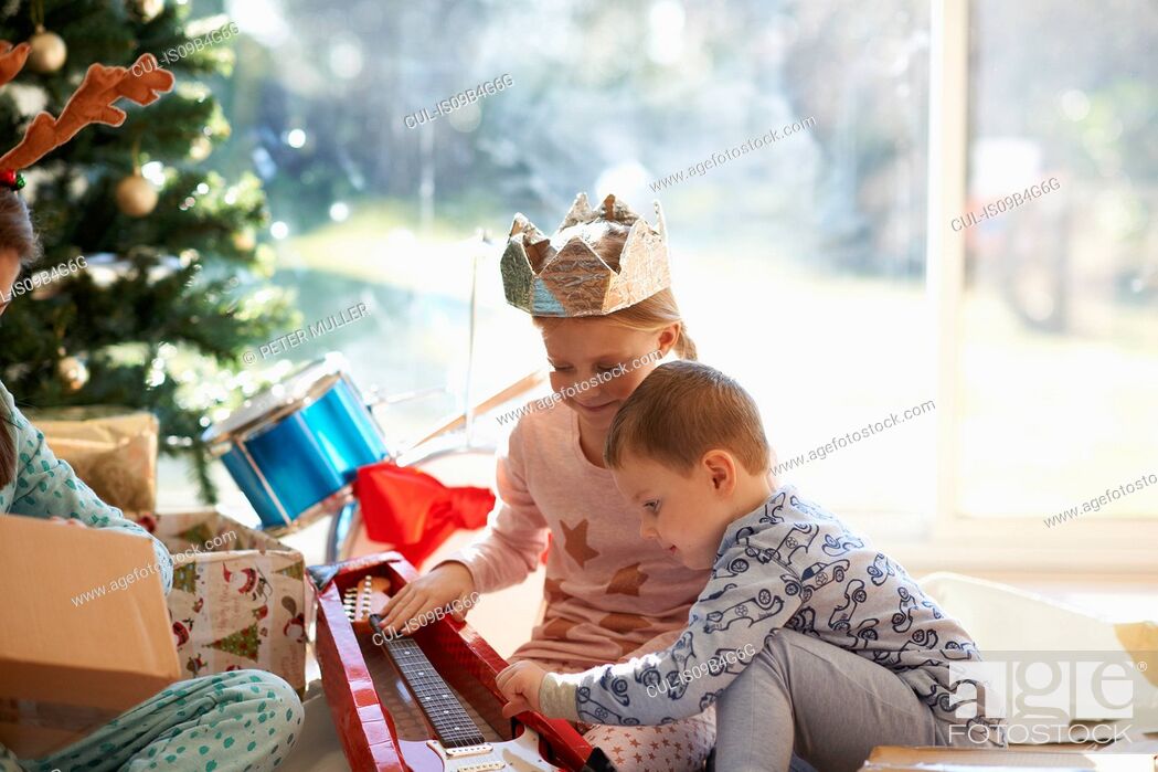 Stock Photo: Girl and brother on living room floor looking at toy guitar christmas gift.
