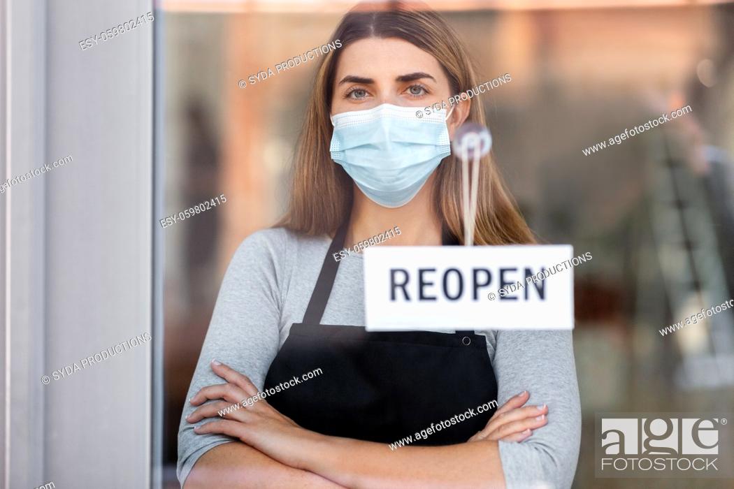 Stock Photo: woman in mask with reopen banner on door glass.