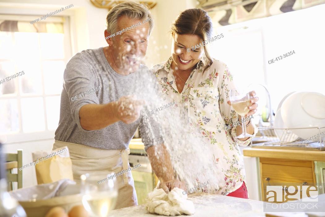 Stock Photo: Playful mature couple baking, throwing flour and drinking wine in kitchen.