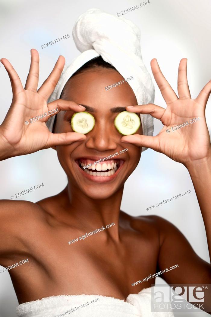 Stock Photo: Close-up portrait of a beautiful smiling woman with clean skin covering eyes with cucumbers isolated on white background.