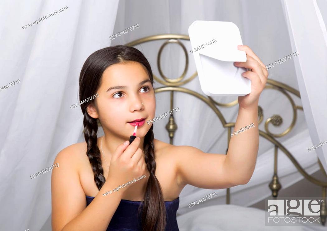 Photo de stock: little girl sitting on a bed looks in the mirror and painting lips like her mom.