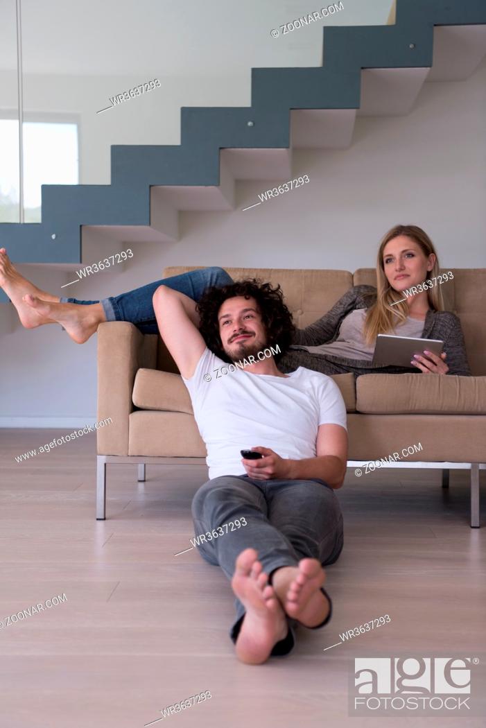 Stock Photo: Young couple relaxes on the sofa in the luxury living room, using a tablet and remote control.