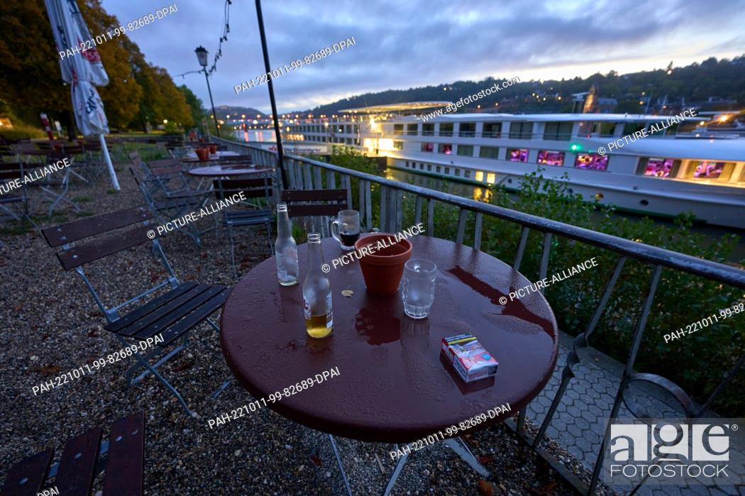 Stock Photo: 11 October 2022, Rhineland-Palatinate, Koblenz: Bottles and glasses from the night before are still on the table of a beer garden in the Rhine area of Koblenz.