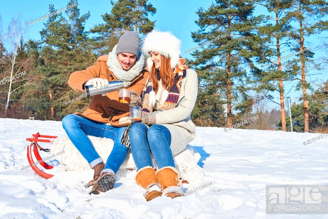 Stock Photo: Glückliches Paar sitzt auf einem Schlitten und trinkt Tee zusammen im Schnee.