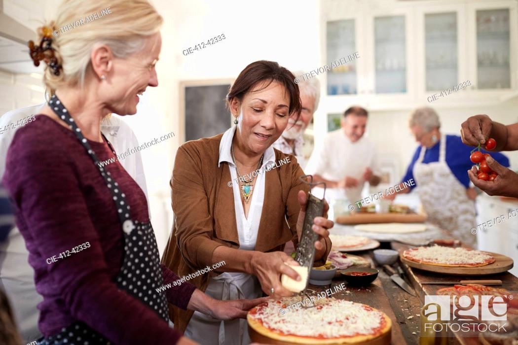 Stock Photo: Senior women friends grating cheese over pizza in cooking class.