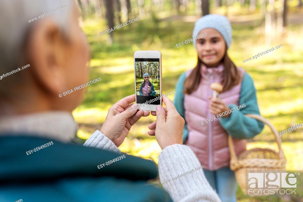 Stock Photo: grandma photographing granddaughter with mushrooms.