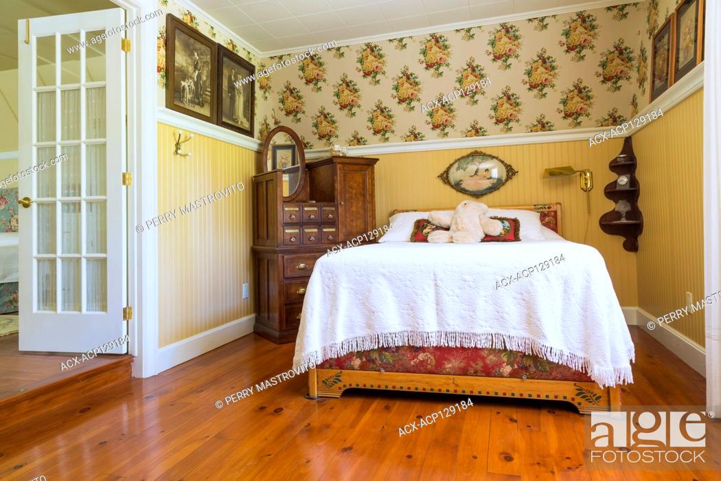 Stock Photo: 1930s double bed with pinewood headboard and white bedspread, antique burled maple pulaskis apothecary bureau, stained and oiled pinewood floorboards in guest.