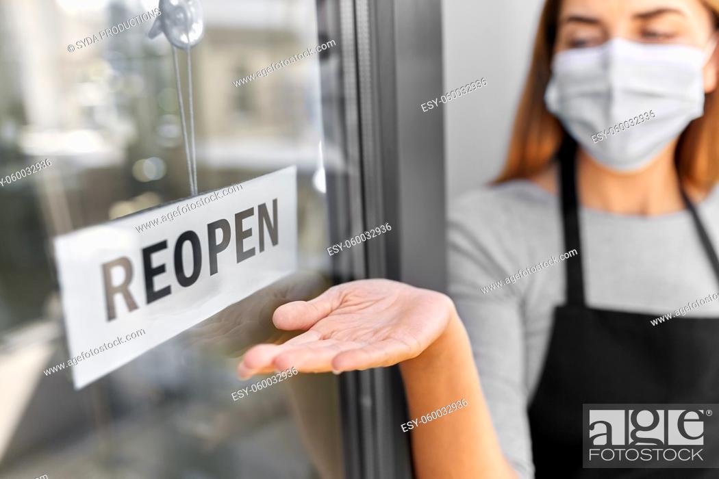 Stock Photo: woman in mask showing reopen banner on door glass.
