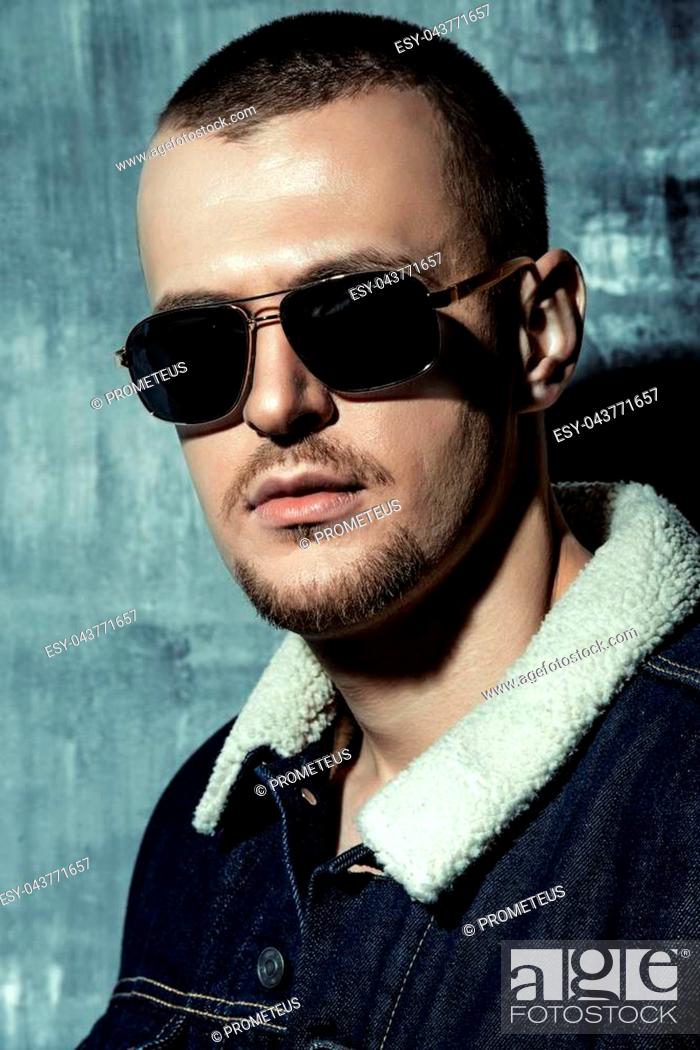 Stock Photo: Sexual male model posing in jeans clothes and sunglasses. Short hair styling. Studio fashion shot.