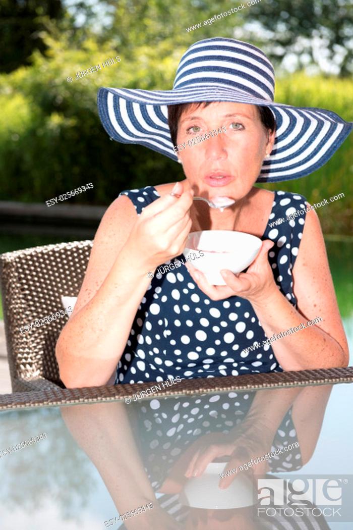 Stock Photo: attractive woman siiting by the pool and eating a bowl of fruit.