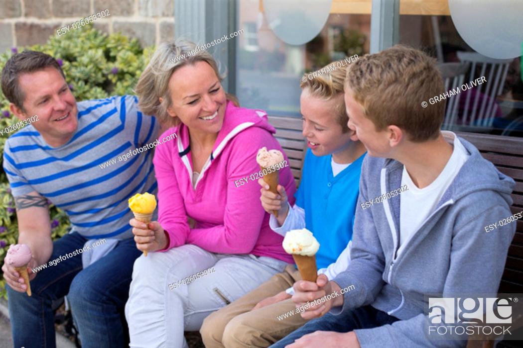 Stock Photo: Family of four enjoying ice cream outside of a shop. They are all wearing casual clothing and holding their ice cream cones.