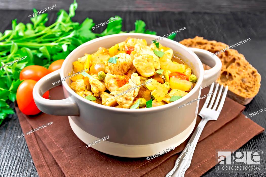 Stock Photo: Stew of chicken breast, tomatoes, stalked celery, carrots, green peas and onions in a tureen on a napkin against dark wooden board.
