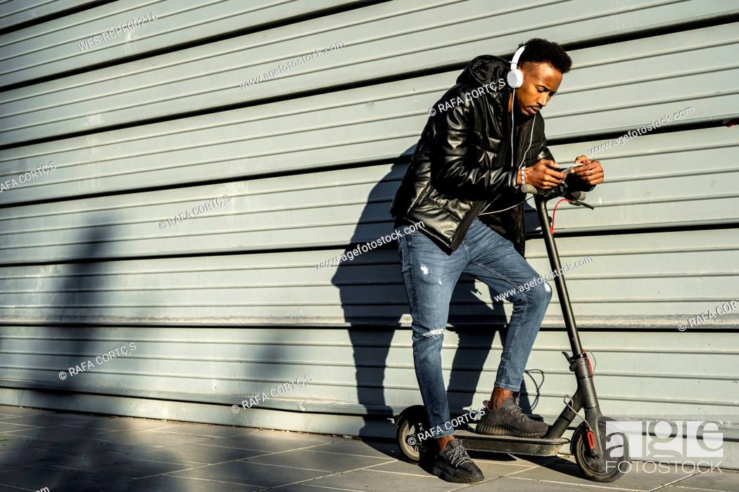 Stock Photo: Man with headphones, smartphone and e-scooter outdoors.