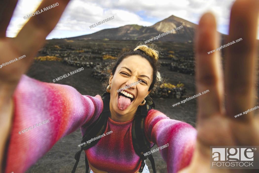 Stock Photo: Happy woman sticking out tongue and taking selfie with landscape in background.
