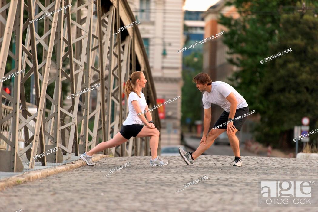 Photo de stock: jogging couple warming up and stretching before morning running training workout in the city with sunrise in background.
