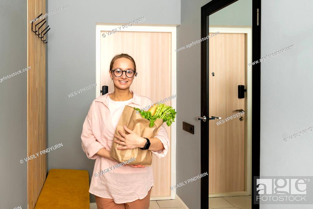 Stock Photo: Smiling woman holding vegetables in paper bag at home.
