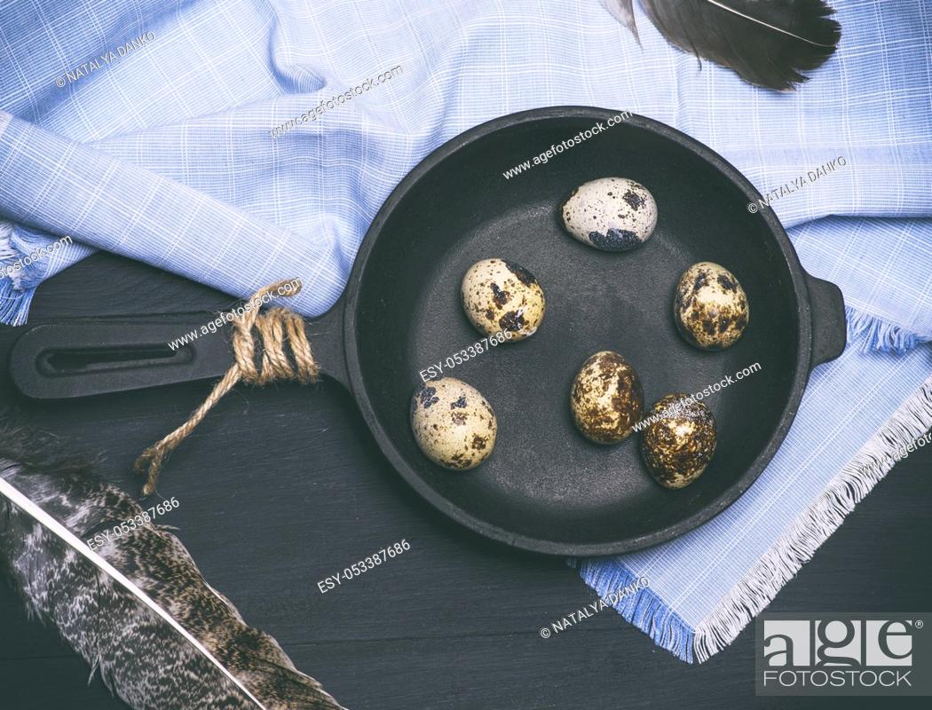 Stock Photo: raw quail eggs in the shell lie in a black cast-iron frying pan, top view.