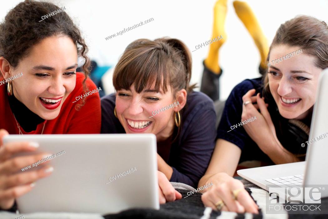 Stock Photo: Laughing young women friends hanging out, enjoying digital tablet and laptop on bed.