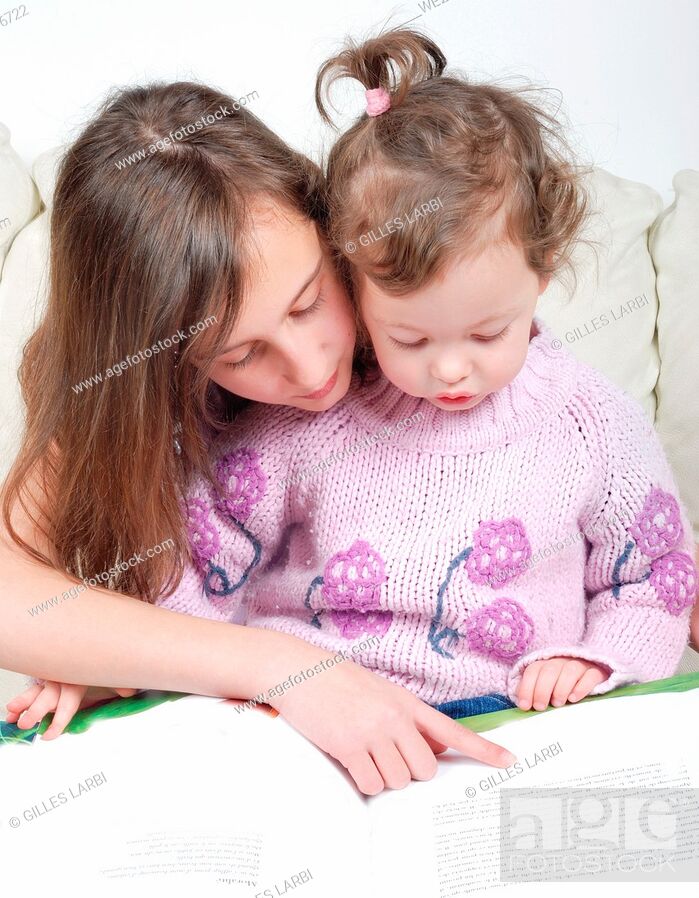 Stock Photo: Sisters sitting in living room reading book.