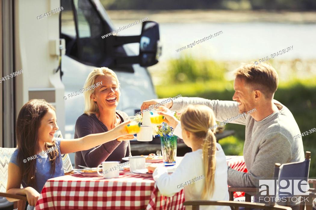 Stock Photo: Family toasting coffee and orange juice glasses at table outside sunny motor home.