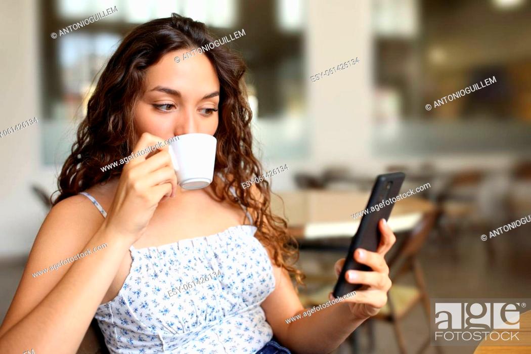 Stock Photo: Woman drinking coffee and checking smart phone sitting in a bar.