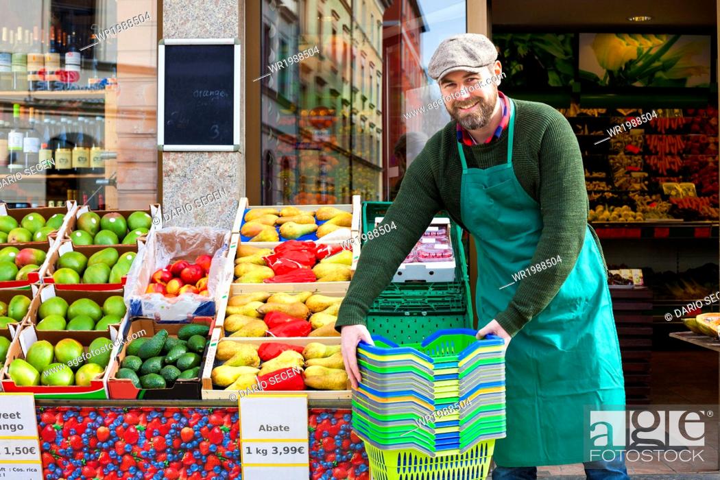 Imagen: Grocer arranging shopper baskets in front of greengrocer's shop.