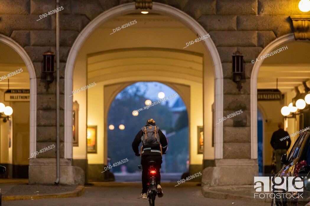 Stock Photo: Copenhagen, Denmark Bicyclists at night pass an arched passageway and a sign for the local Det Nu Teater theatre in downtown.