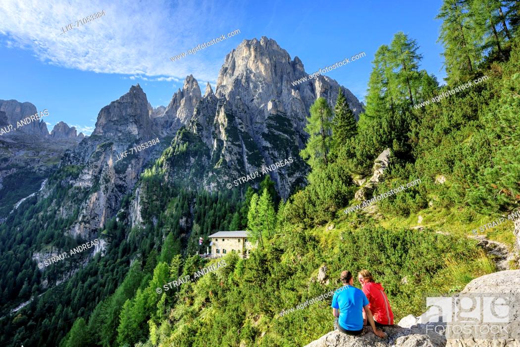 Stock Photo: Two persons hiking sitting on rock in front of hut Rifugio Treviso with Cima dei Lastei, valley Val Canali, Pala range, Dolomites.