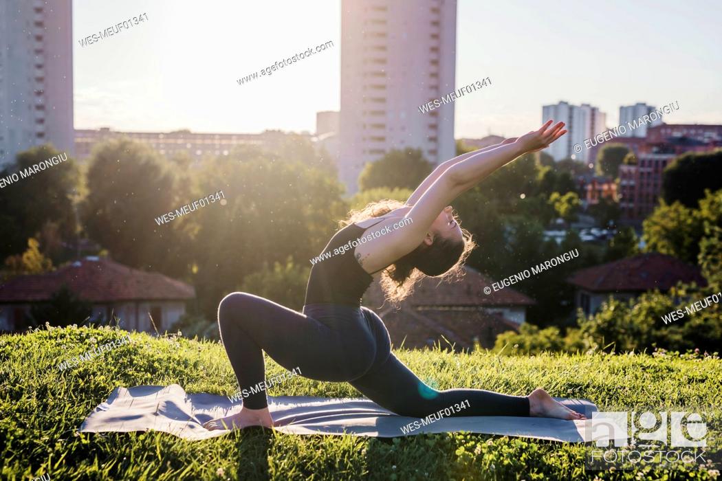 Stock Photo: Young woman practicing yoga in warrior position at city park during sunny day.