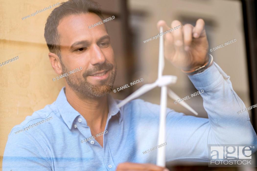 Stock Photo: Businessman with wind turbine model behind windowpane.