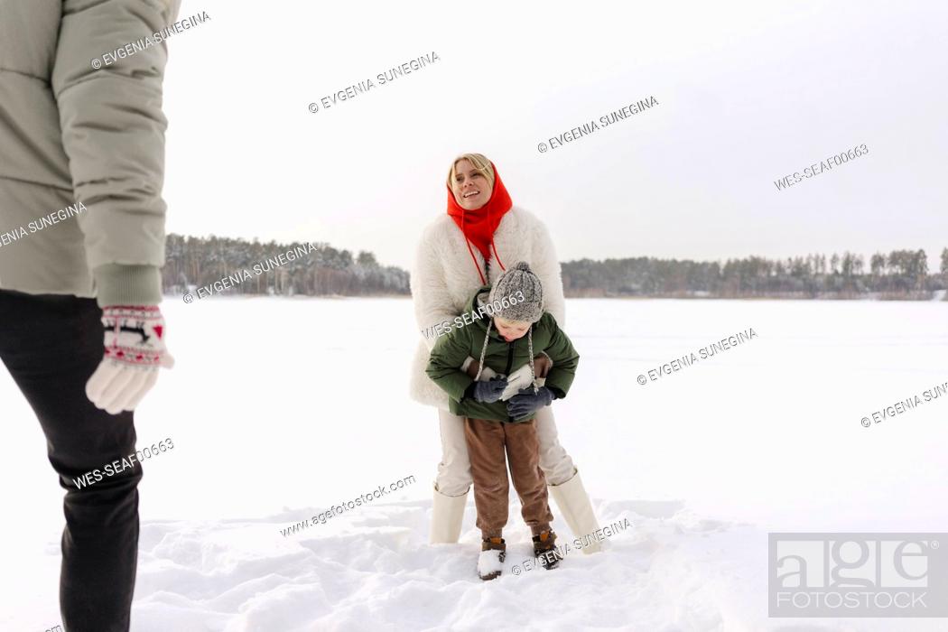 Photo de stock: Smiling woman embracing son looking at man standing on snow.