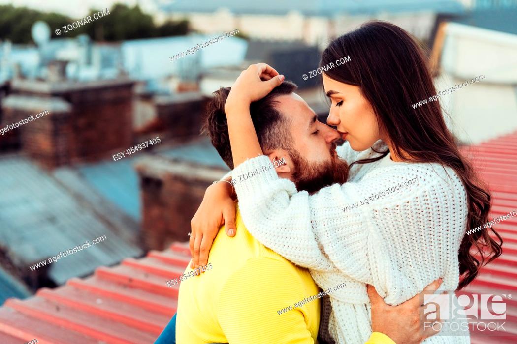 Stock Photo: Loving young couple is sitting on the roof of the house. In the background of a big city house.