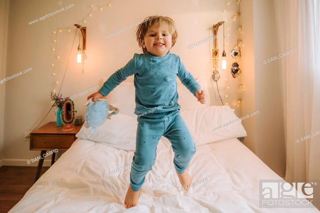 Stock Photo: little blond boy has fun jumping and playing on a big bed. family at home. coronavirus. quarantine.