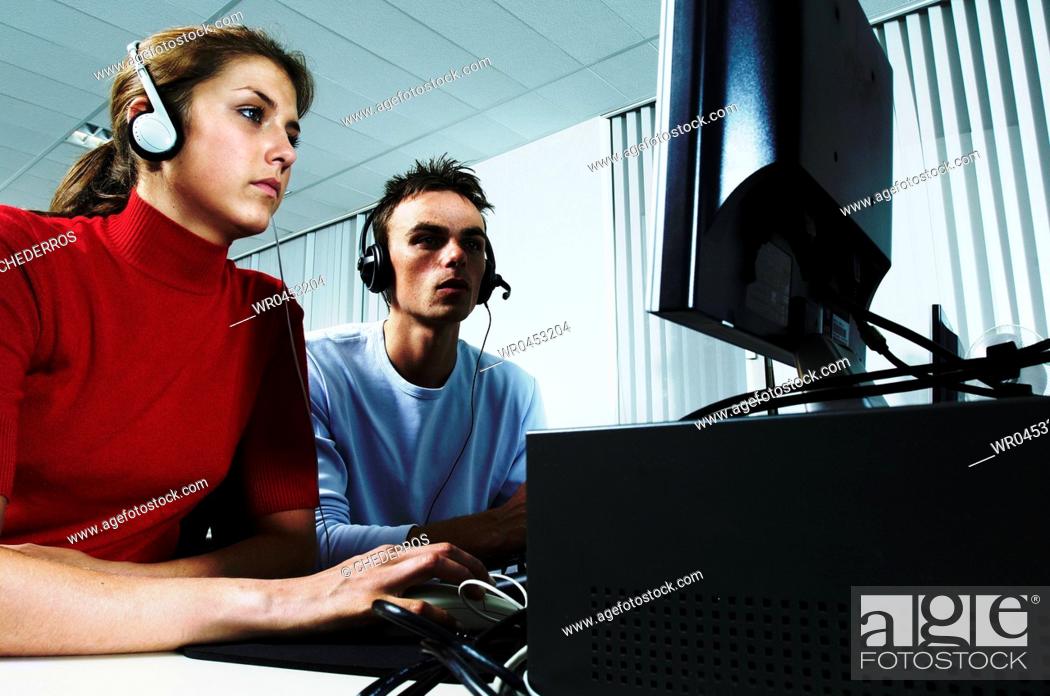Stock Photo: Teenage girl wearing headphones using a computer with a teenage boy sitting beside her.