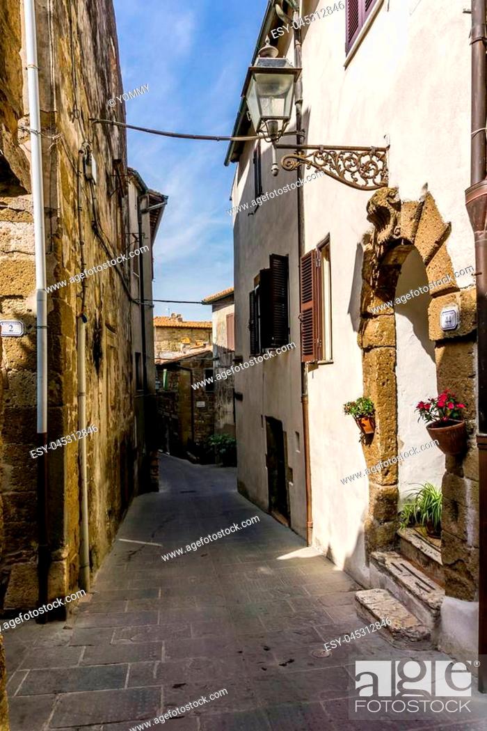 Stock Photo: Vertical photo with view into narrow ancient street in the Pitigliano historic town. Town is located in Italy Tuscany. Old stone road is between houses build.