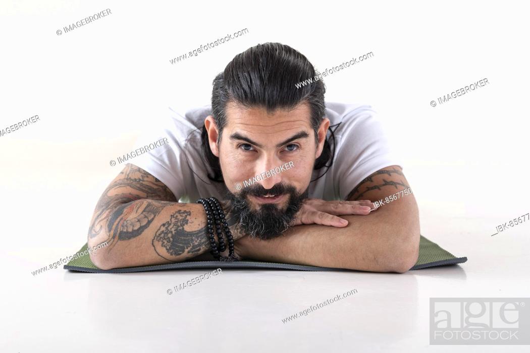 Photo de stock: Portrait of a man dressed in white yoga clothes lying on a mat while looking at camera over white background. Studio shot.