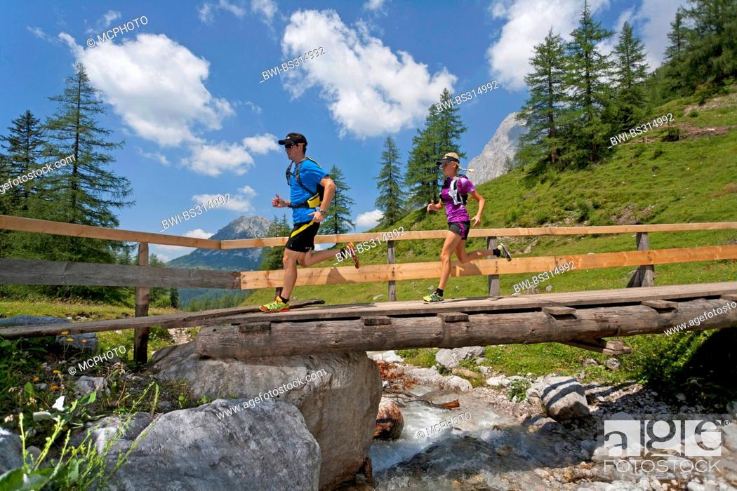 Stock Photo: young couple running over a wooden bridge over a brook while trail running in the Dachstein Mountains, Austria, Styria, Dachstein.