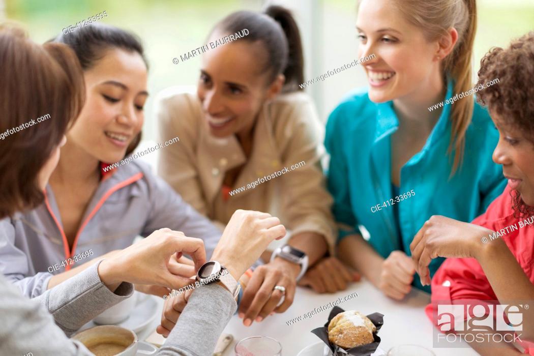 Stock Photo: Smiling women friends looking at smart watches in cafe.
