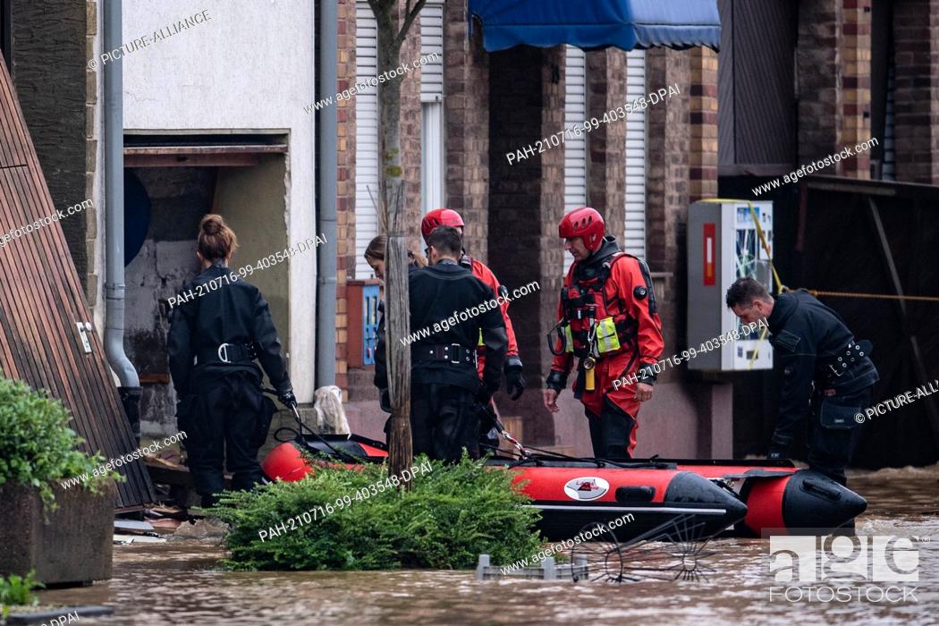 Stock Photo: 16 July 2021, North Rhine-Westphalia, Landesweit: Lifeguards and police divers go into a flooded courtyard in an inflatable boat.