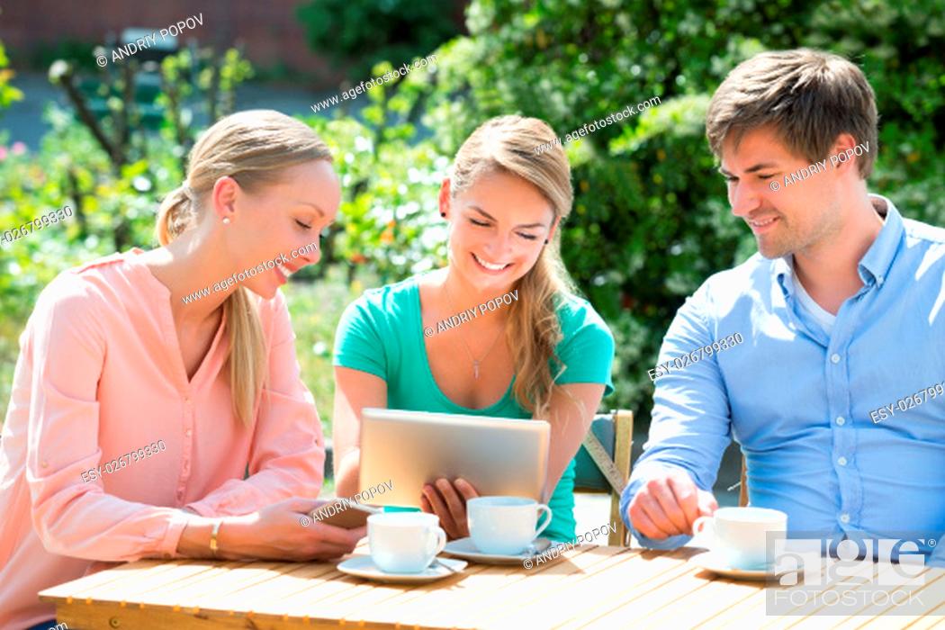 Stock Photo: Group Of Smiling Friends Looking At Digital Tablet With Cup Of Coffee On Table.