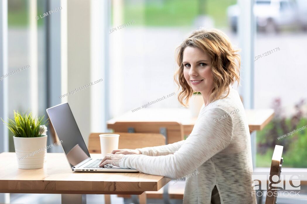 Stock Photo: A professional business woman working on a computer in a coffee shop and stopping to look at the camera: Edmonton, Alberta, Canada.
