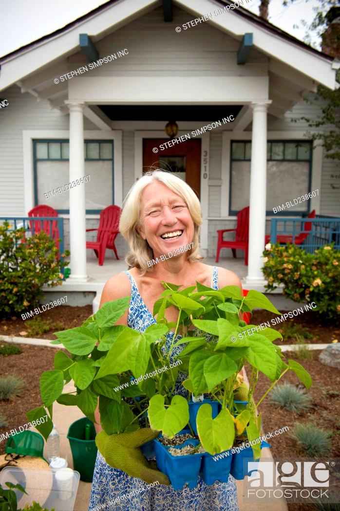 Stock Photo: Portrait of smiling Caucasian woman holding tray of plants near house.