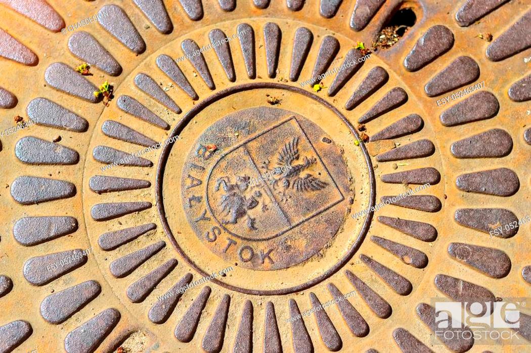 Stock Photo: Old cast iron sewerage hatchway cover with the coat of arms of city Bialystok, Poland. Iron manhole on the road of the big city.