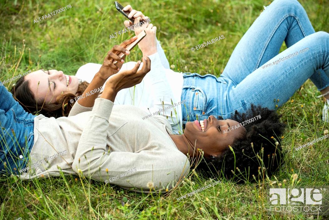 Photo de stock: Young female friends lying on grass while using smart phone in park.