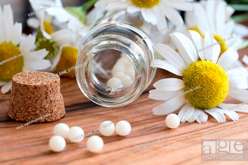 Stock Photo: A bottle of homeopathic globules with chamomile flowers in the background.