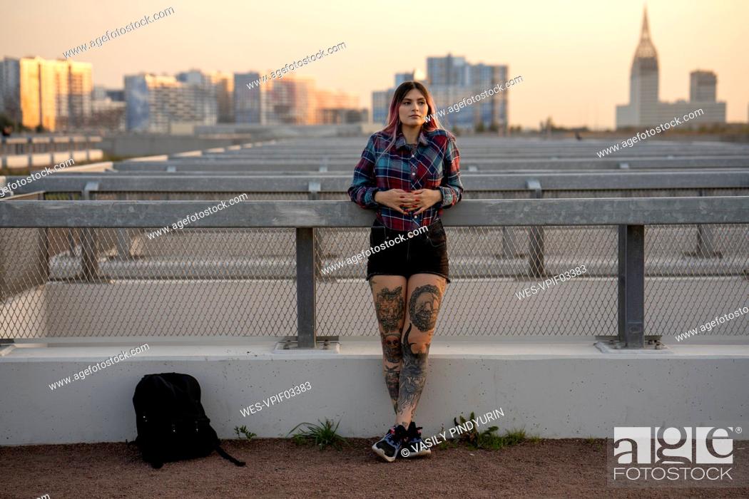Stock Photo: Fashionable woman day dreaming while leaning on railing at rooftop during sunset.