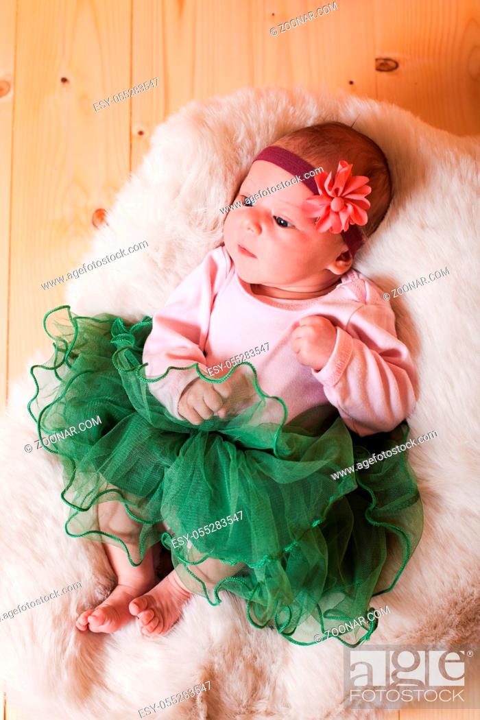 Stock Photo: Newborn baby girl in green tutu is lying on the fur.