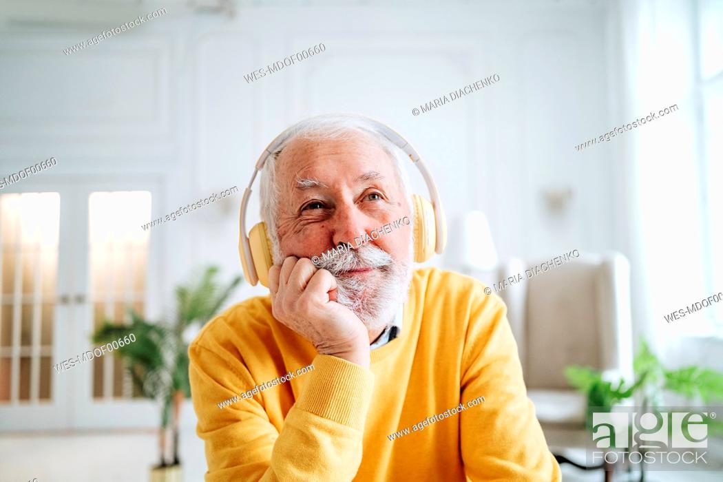 Imagen: Thoughtful senior man listening to music through headphones at home.