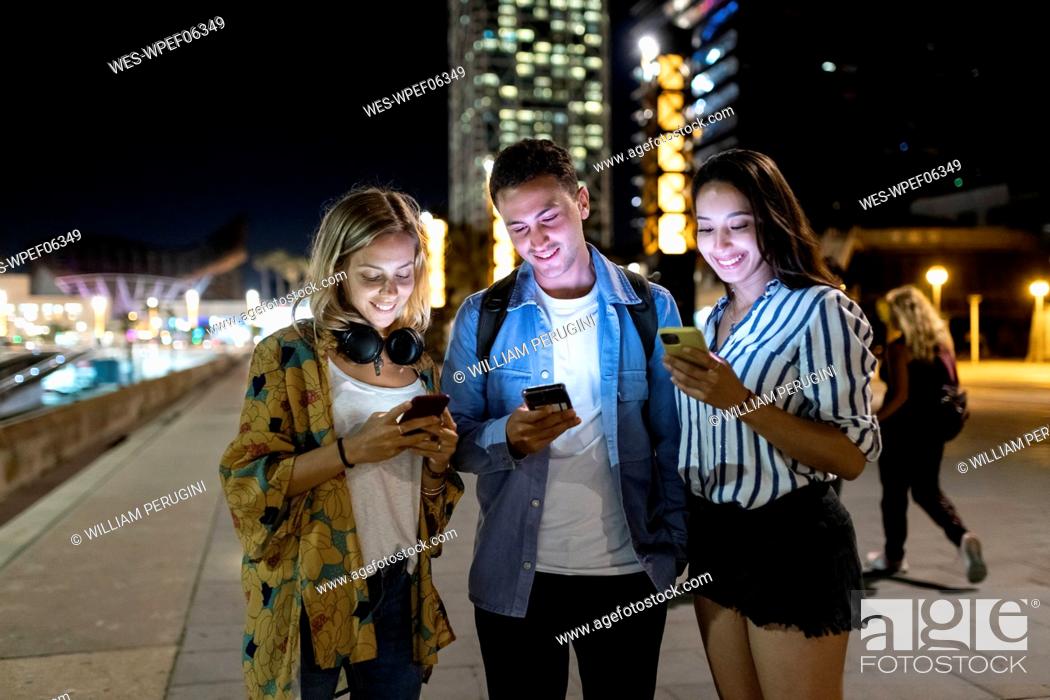 Stock Photo: Smiling man and women surfing net through smart phone in city.