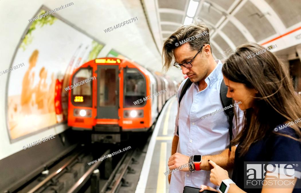 Stock Photo: UK, London, couple waiting at  underground station platform looking at smartwatch.